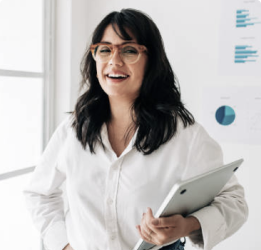 A woman wearing glasses holding a laptop and smiling