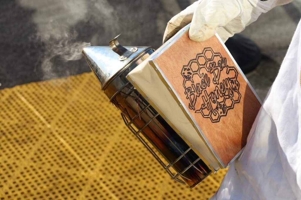 An image of a beekeeper whose bee smoker reflects a Black Bee Honey logo