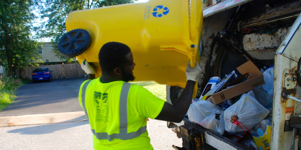 Garbage collector in a yellow vest loading a garbage can