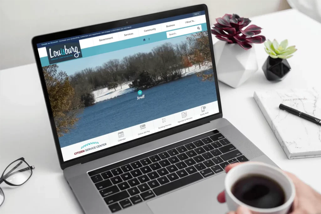 A laptop displays the homepage of Louisburg, Kansas