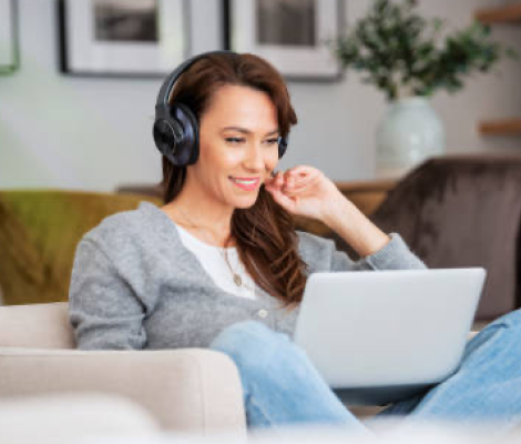 Woman sitting on a couch, wearing headphones and working on a laptop