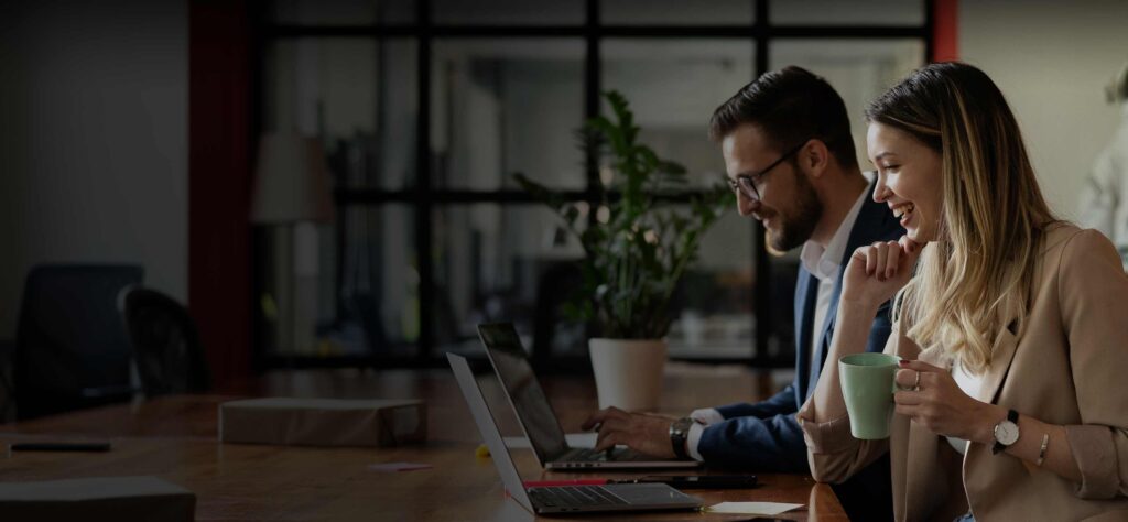 Man and woman looking at their laptop screens and smiling