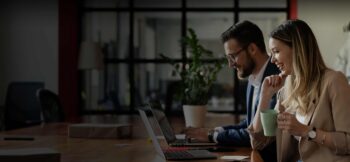 Man and woman looking at their laptop screens and smiling