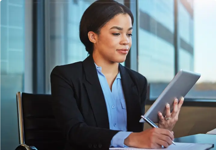 Woman at work holding a tablet in one hand, and writing on a notepad