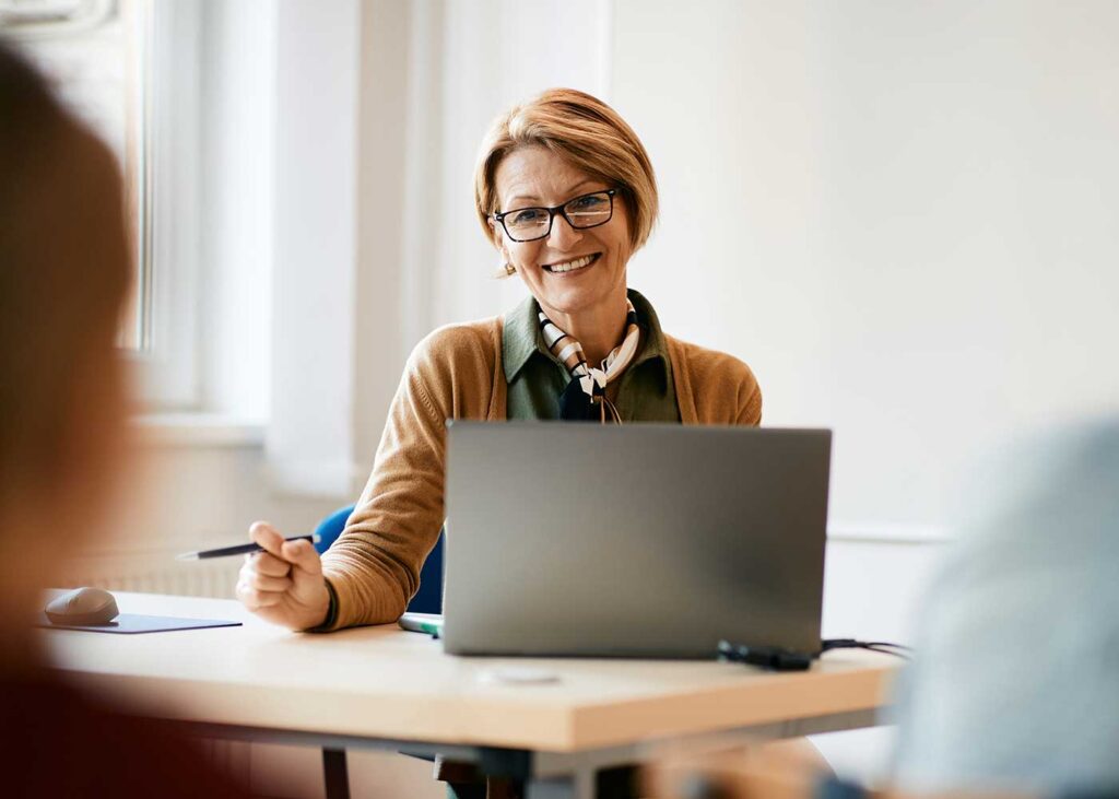 Teacher addressing a class of students and working on her laptop