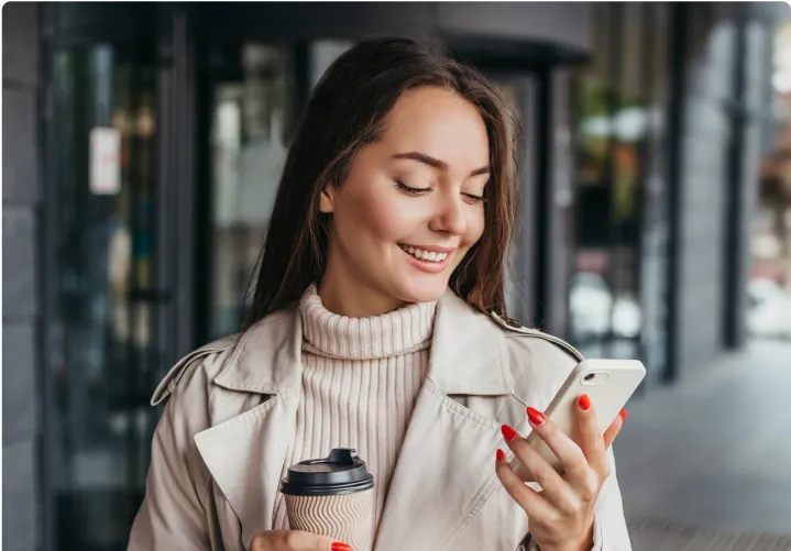 A woman holding a phone and a coffee cup