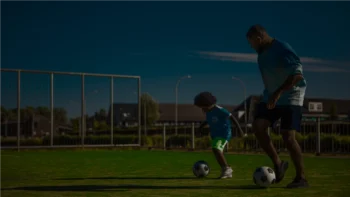 Man and a kid playing soccer in the field