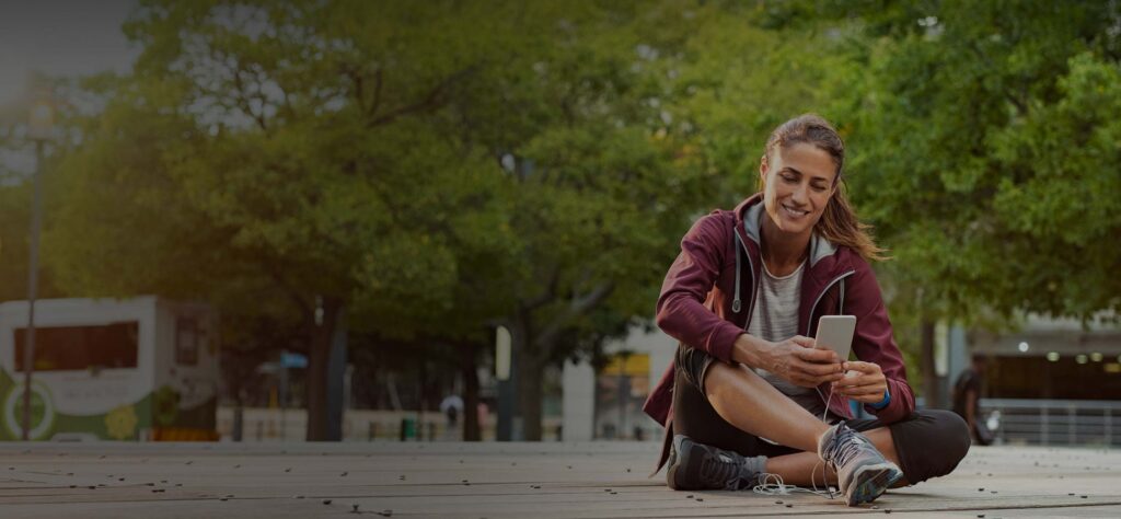 Woman in active gear sitting outside using a phone
