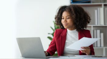 Employee at a desk in a red jacket reviewing laptop
