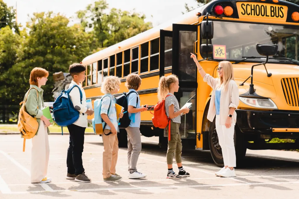 Young Teacher Counting Group Of Kids Pupils Schoolchildren Before Boarding