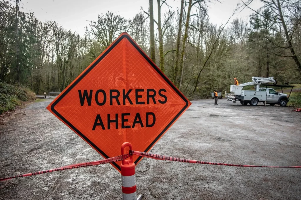 Workers Ahead sign on a road with road repair workers in the background