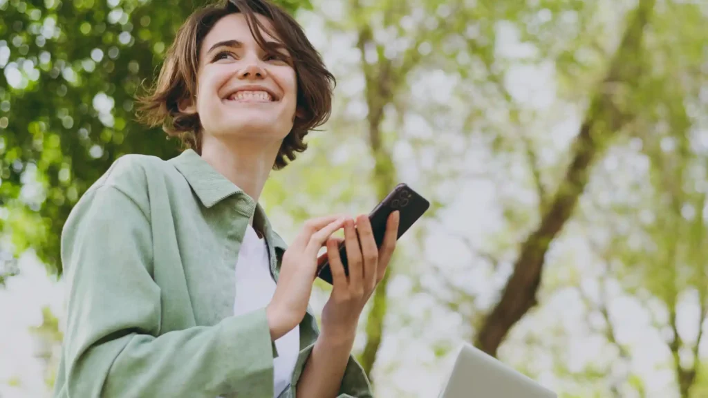woman holding her cell phone in a park