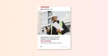 man wearing a construction safety vest and hat holding a roll of paper while smiling, looking at a cell phone in his hand.