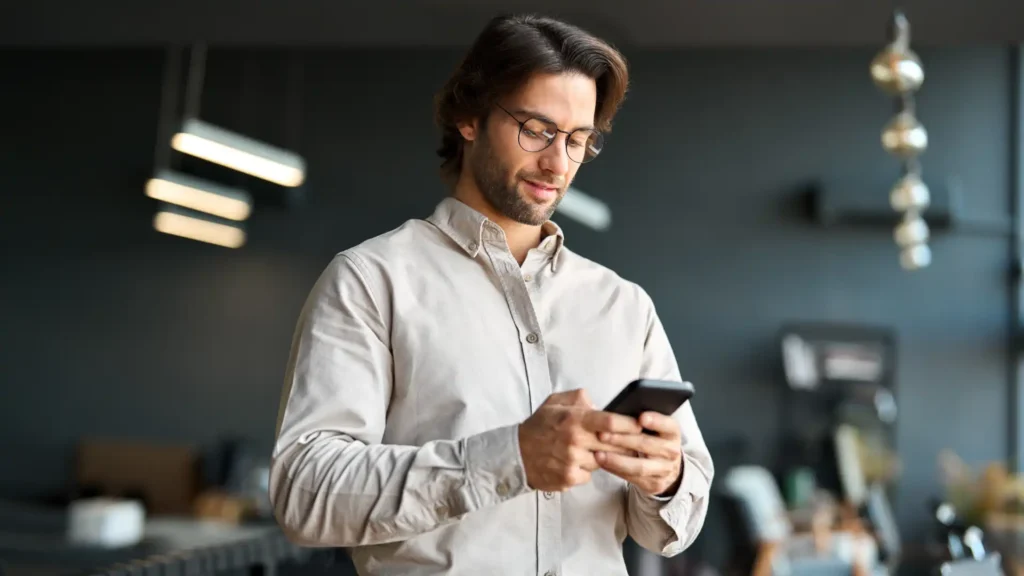 man in an office typing on cell phone