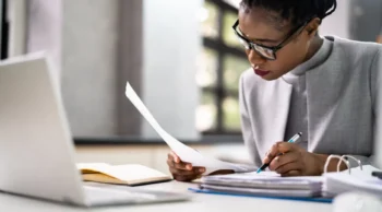 woman reviewing papers by her laptop
