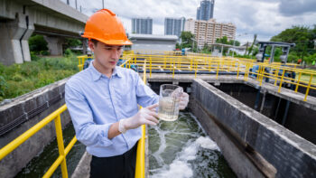 worker in hard hat holding water testing above water treatment