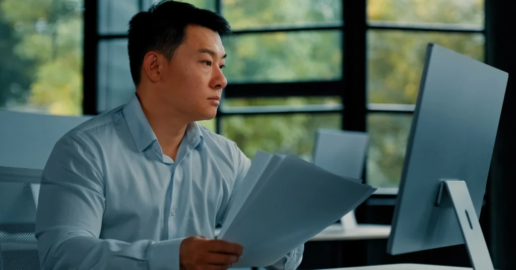 Employee with papers looking at a monitor